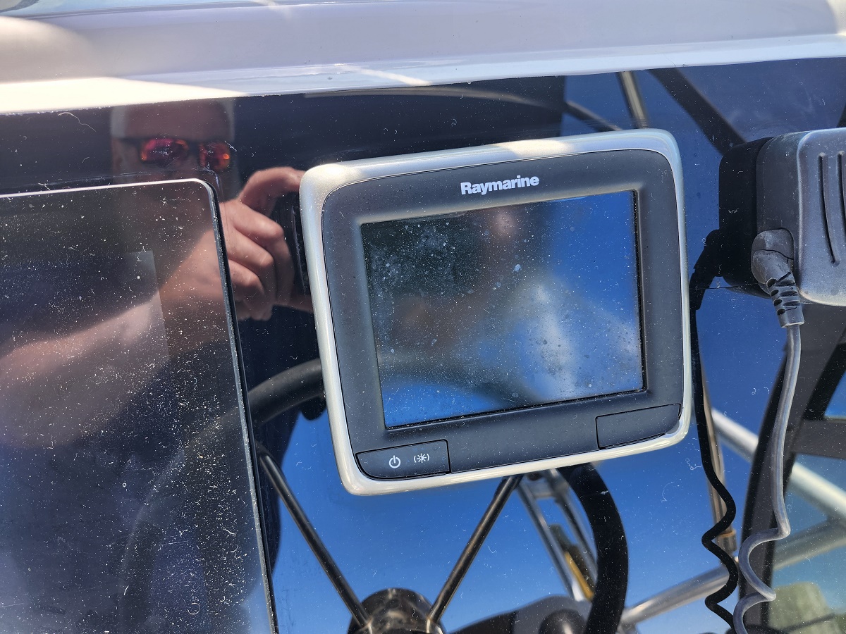 Raymarine marine display mounted on a boat helm with routed cables; photographer's reflection visible in the screen glass.