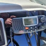 Close-up of a Raymarine VHF marine radio mounted on a boat dashboard with a small display and radio buttons.