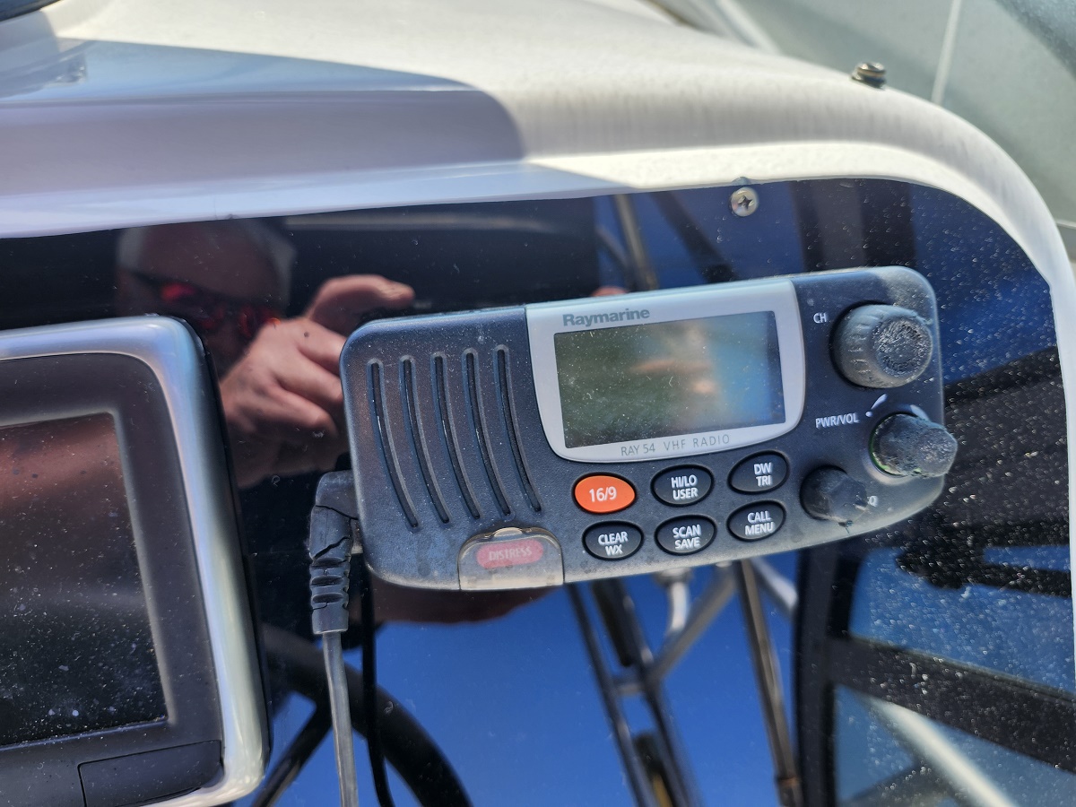 Close-up of a Raymarine VHF marine radio mounted on a boat dashboard with a small display and radio buttons.