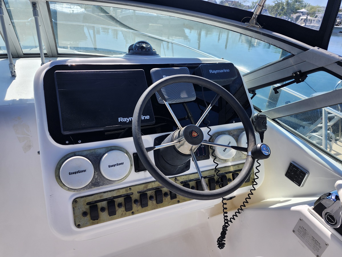 Boat helm with steering wheel and Raymarine displays overlooking calm marina.