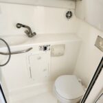 Small boat head: compact white bathroom with sink, metal faucet, toilet, and round vent on wall.
