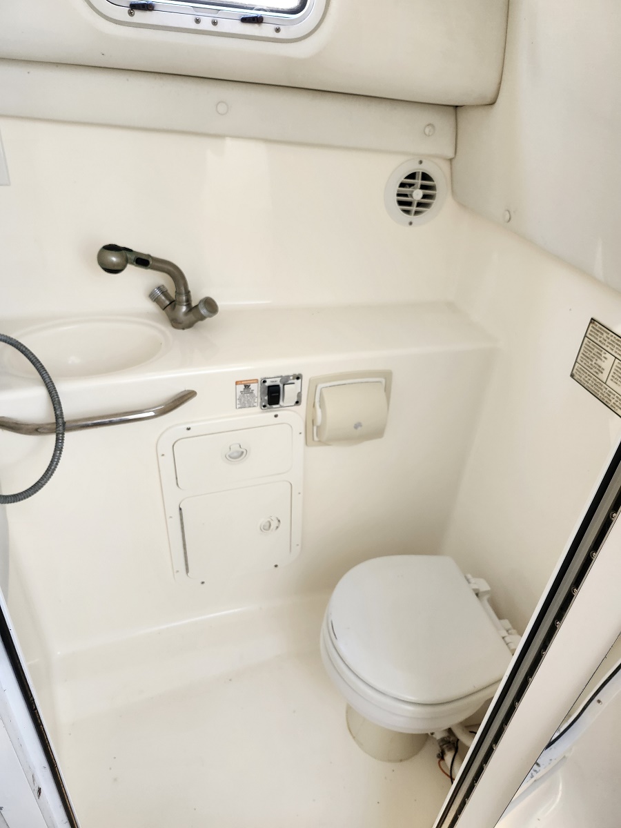 Small boat head: compact white bathroom with sink, metal faucet, toilet, and round vent on wall.