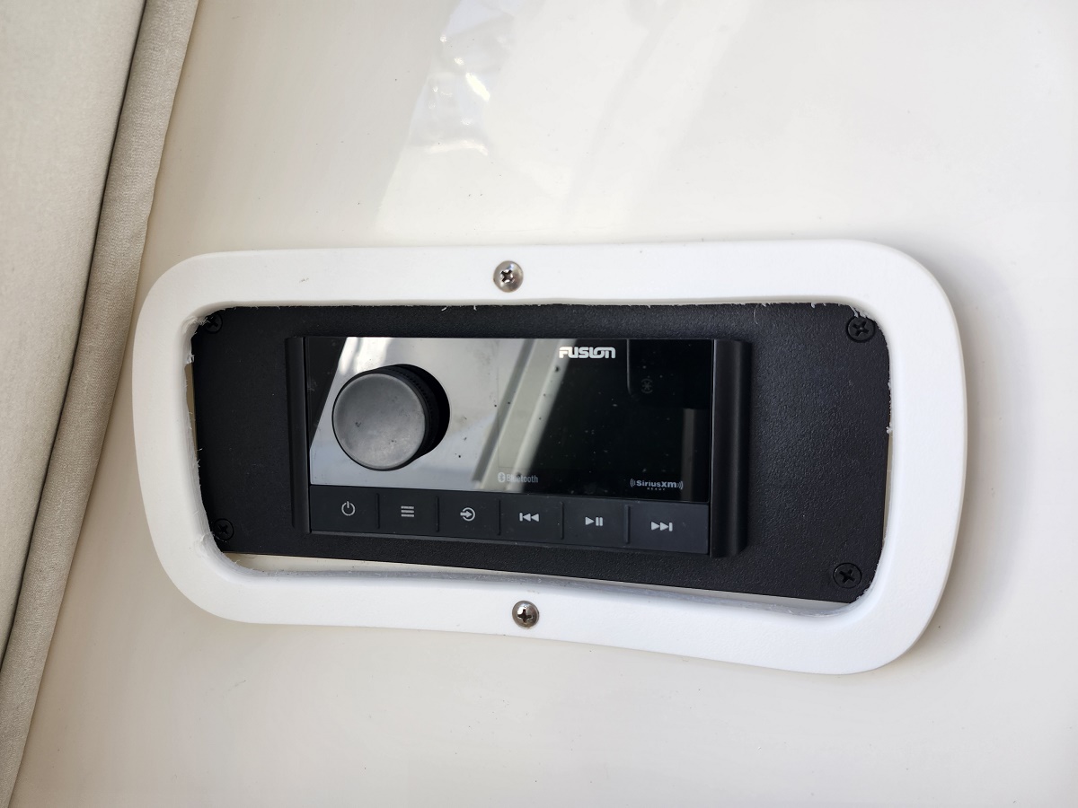 Fusion marine stereo head unit mounted in a white recessed panel, with a large round volume knob and playback buttons