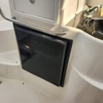 Compact black Norcold refrigerator inset into a boat's white galley wall, with a chrome grab rail above.