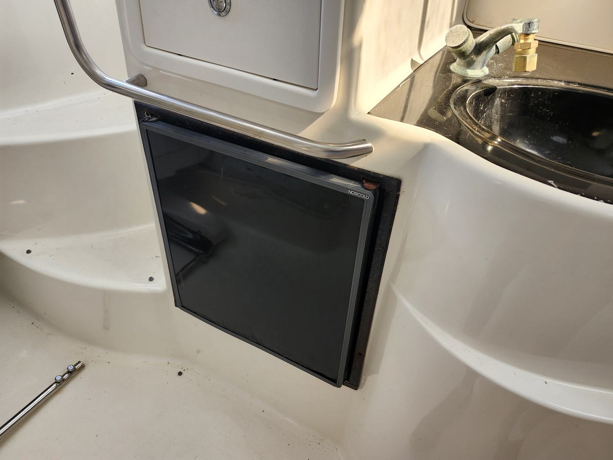 Compact black Norcold refrigerator inset into a boat's white galley wall, with a chrome grab rail above.