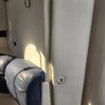 Close-up of a beige padded wall in a vehicle interior, with a blue leather armrest in the lower-left and a circular white fastener on the panel.