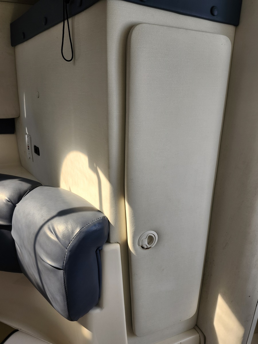 Close-up of a beige padded wall in a vehicle interior, with a blue leather armrest in the lower-left and a circular white fastener on the panel.