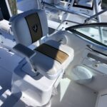 White captain chair with tan stripe in a boat cockpit, logo on backrest, mounted on a pedestal near the helm.