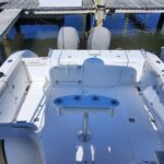 White fishing boat docked at a wooden marina, showing an open cockpit with seating along the sides and twin outboard motors at the stern.