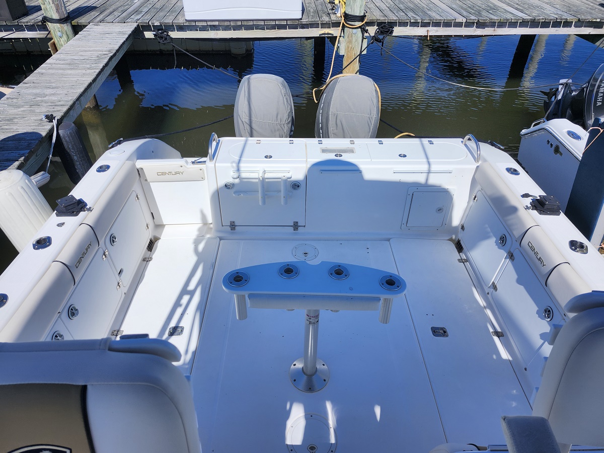 White fishing boat docked at a wooden marina, showing an open cockpit with seating along the sides and twin outboard motors at the stern.