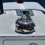 Bow of a boat with a chrome windlass and heavy anchor chain coiled beside it, under bright sunlight