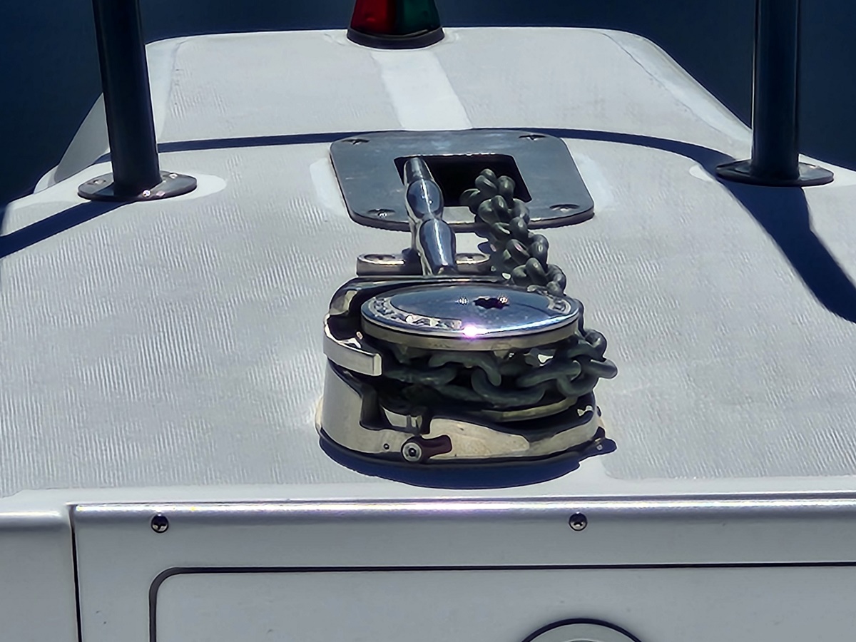 Bow of a boat with a chrome windlass and heavy anchor chain coiled beside it, under bright sunlight