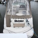 Rear view of a white motorboat named 'NEATSEA' docked at a marina, with a beige canvas canopy and visible cockpit seating.