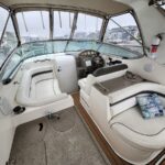 Interior of a white motorboat cockpit featuring a wood steering wheel, instrument panel, and beige seats, with marina view outside.