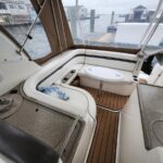 White U-shaped boat seating with a small oval table on a teak deck; marina docks visible through clear enclosure behind.