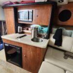 Compact RV kitchen with microwave, wooden cabinets, sink, and small fridge.