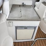 Boat galley with granite countertop, sink, stove covers, and a small front-access fridge beneath; teak deck flooring visible nearby