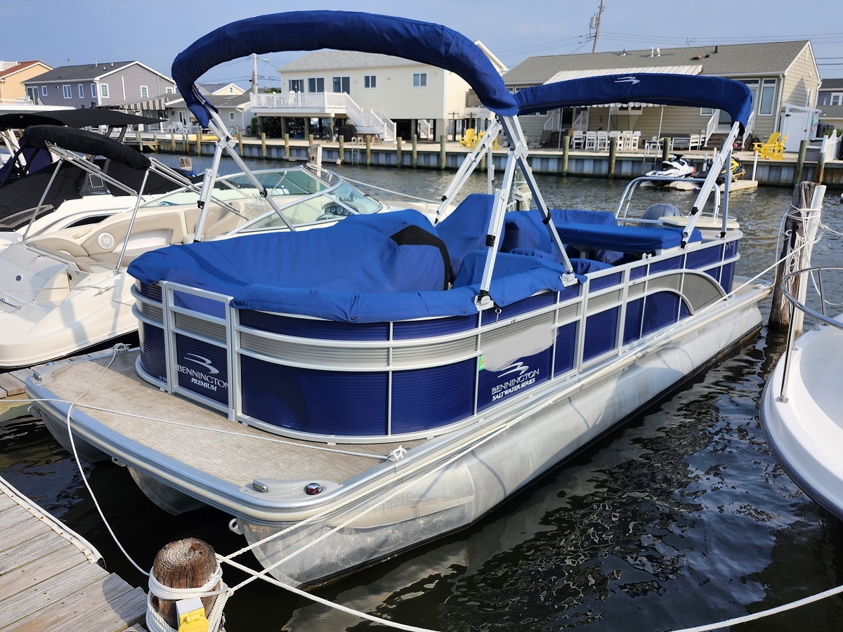 20260811_091913 - Ocean Beach Marine Centers Blue pontoon boat with a blue canopy docked at a marina, white railings and houses in the background
