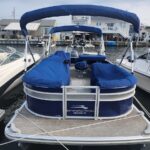 Blue Bennington Premium pontoon boat docked at a marina, with blue canvas covers on seating and canopy, surrounded by other boats and waterfront houses.