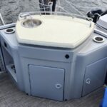 Boat deck console with a small round sink and faucet on a light countertop, surrounded by storage cabinets and cup holders.