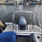 Rear view of a small pontoon boat tied at a marina, with a gray Yamaha outboard motor, railing, and water in the background