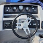 Boat helm with black steering wheel, four gauge dials, and Garmin display panel.