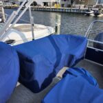 Blue-covered seating on a docked boat at a marina, with neighboring boats and waterfront houses in the background.