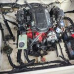 Boat engine compartment with a Volvo Penta inboard engine, battery, hoses, and wiring visible in a tight bilge space