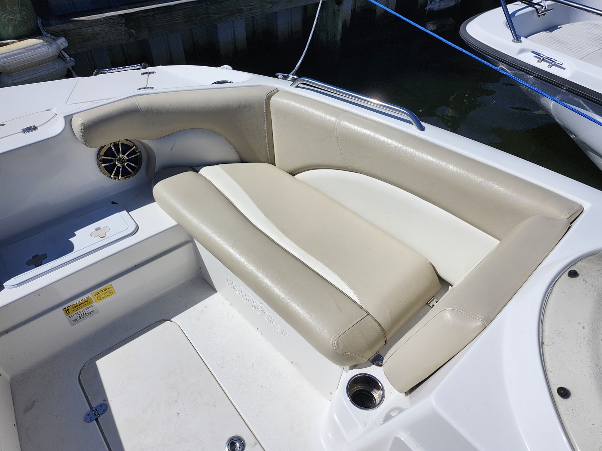White motorboat cockpit with tan cushioned U-shaped seating and a built-in cup holder by the water's edge at a marina