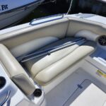 Cockpit seating on a white boat with beige cushioned benches and two metal rods resting on the seatback next to a round speaker.