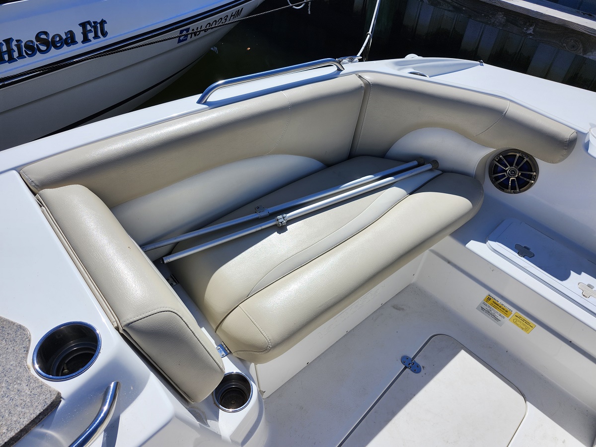 Cockpit seating on a white boat with beige cushioned benches and two metal rods resting on the seatback next to a round speaker.