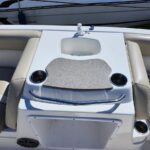 Boat cockpit centerpiece: small sink with faucet, two cup holders, and a textured cover on a white console between beige seats.
