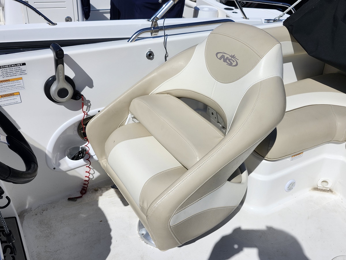 Beige and white captain's chair on a boat deck, mounted beside the console with a red lanyard nearby.