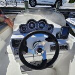 Steering wheel and dashboard of a small motorboat with analog gauges and a mounted Lowrance display on the right.