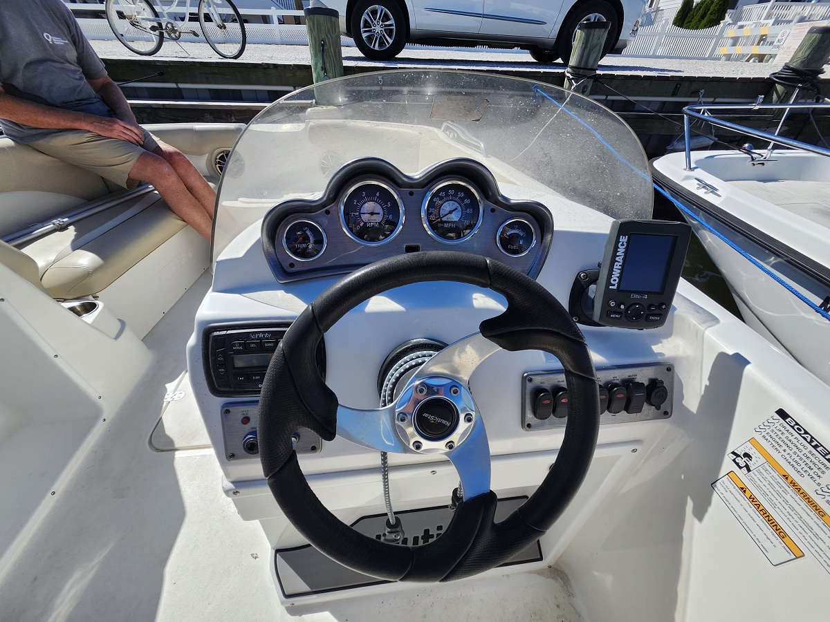 Steering wheel and dashboard of a small motorboat with analog gauges and a mounted Lowrance display on the right.