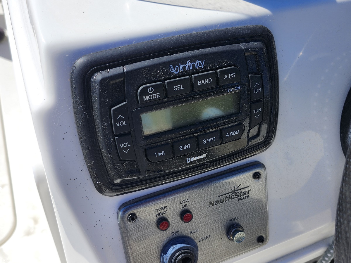 Boat radio console with Infinity stereo and control buttons mounted on a white boat panel, Bluetooth enabled display visible beside climate dust.