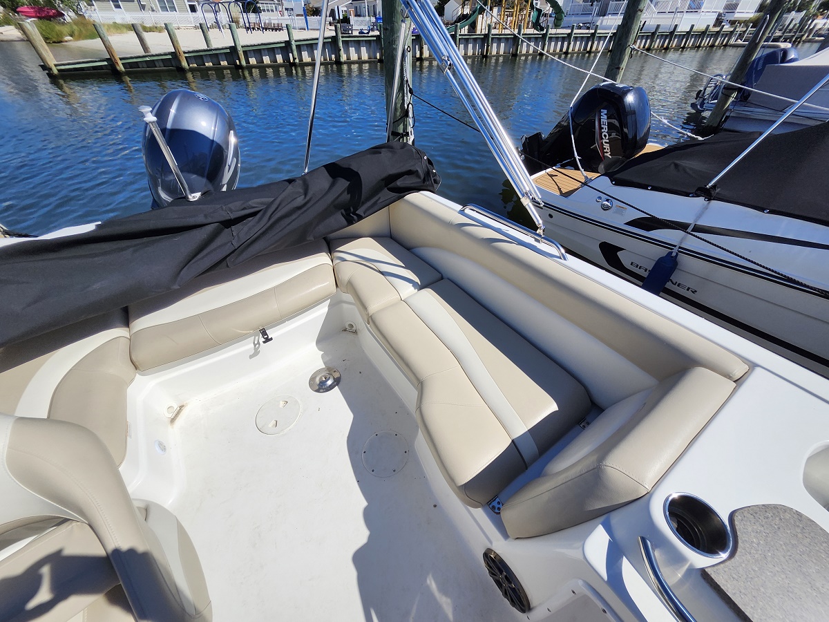 Open cockpit of a white boat with tan cushioned seating, dock and another boat visible in the marina.