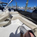 Interior of a small motorboat with beige cushioned seating, docked in a marina under a bright blue sky.