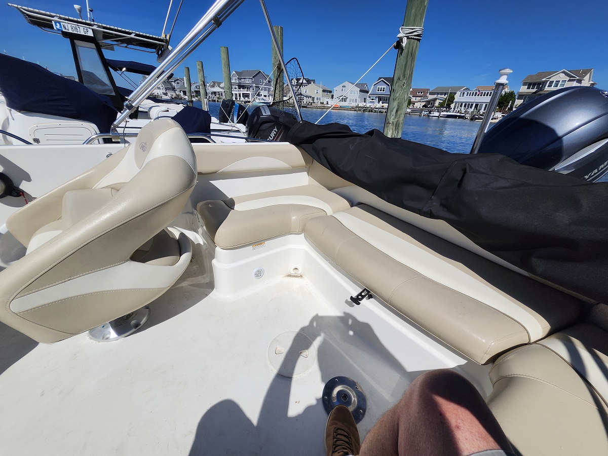 Interior of a small motorboat with beige cushioned seating, docked in a marina under a bright blue sky.