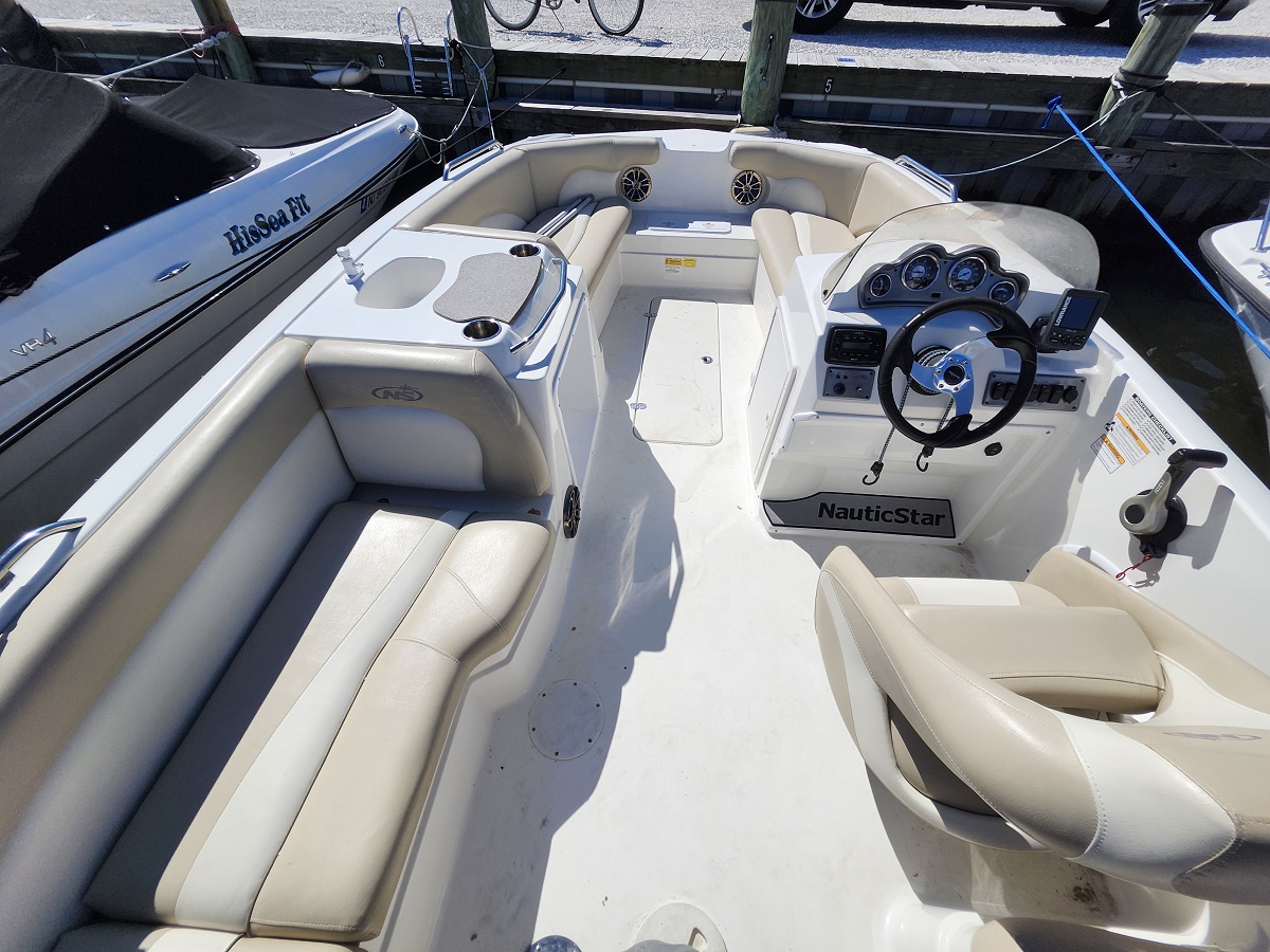 NauticStar center-console boat cockpit with beige cushioned seating and steering wheel, dock mooring visible outside.