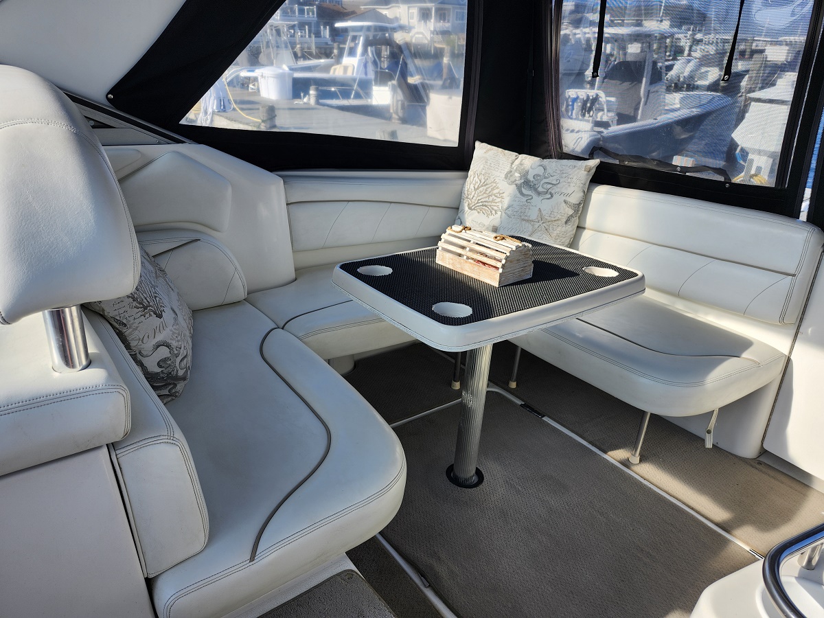 White leather boat seating around a rectangular table with a small wooden centerpiece; marina visible through the large windows.