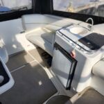 White leather boat seating surrounds a central console with a small sink and built-in compact refrigerator; a dark non-slip mat rests on the counter and sandals lie on the deck nearby.