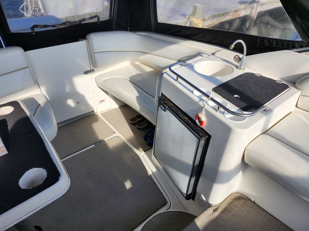White leather boat seating surrounds a central console with a small sink and built-in compact refrigerator; a dark non-slip mat rests on the counter and sandals lie on the deck nearby.