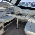 White leather yacht seating around a small pedestal table, with a decorative wooden chest in the center; docked boats visible through the windows.