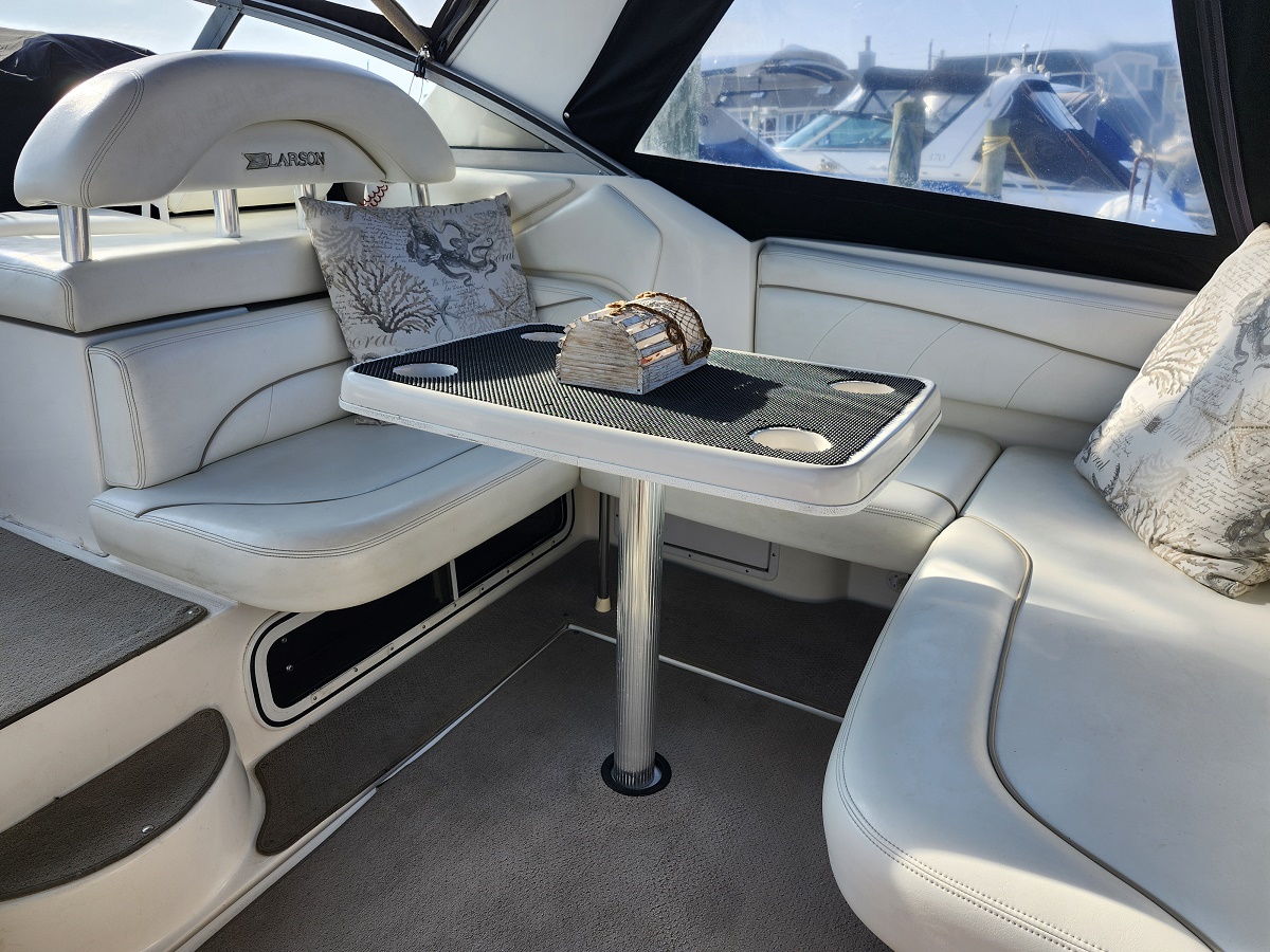 White leather yacht seating around a small pedestal table, with a decorative wooden chest in the center; docked boats visible through the windows.