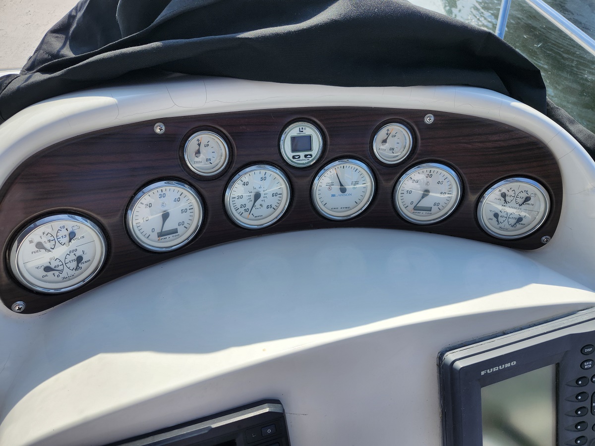 Boat dashboard with multiple round gauges on a wood-panel background, partially covered by a black canvas cover.