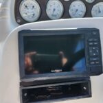 Garmin marine GPS display mounted on a boat console with round gauges in the background.