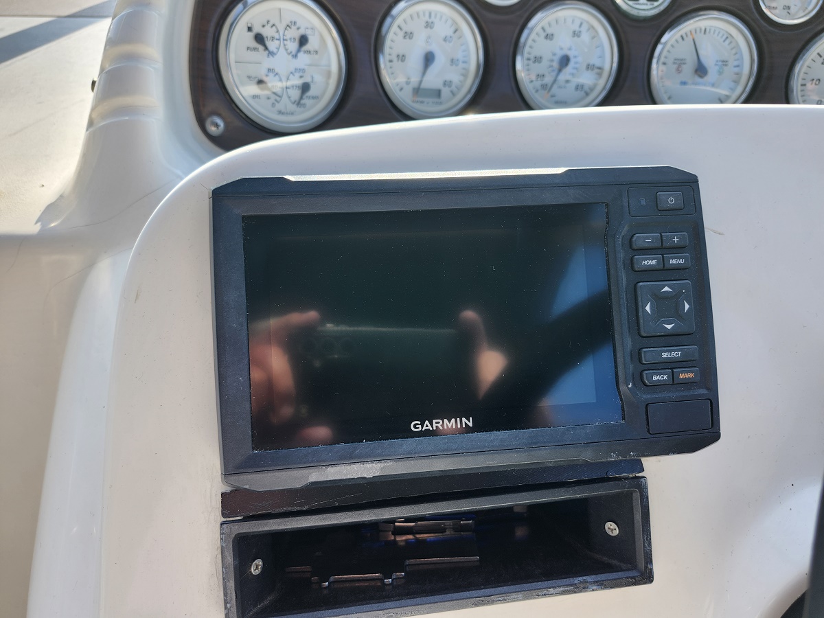 Garmin marine GPS display mounted on a boat console with round gauges in the background.