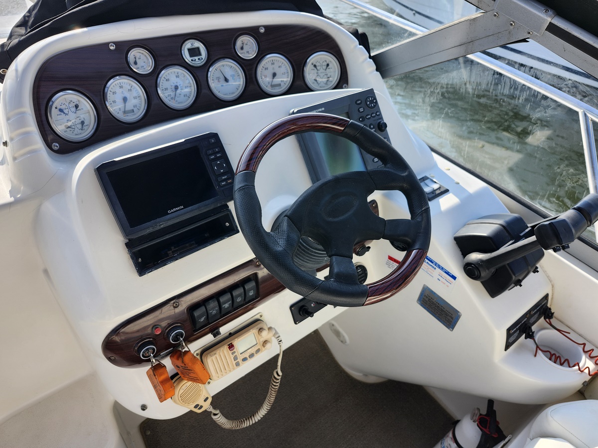 Boat helm with steering wheel, gauges, and Garmin navigation screen on white console.