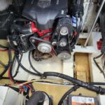 Boat engine bay with a red-and-black V-style engine, belts, pulleys, hoses, and wiring visible on a yellow deck.